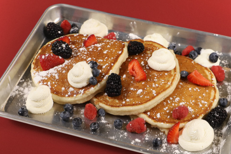 pancakes with strawberries, blackberries, blueberries, and whipped cream on a metal plate